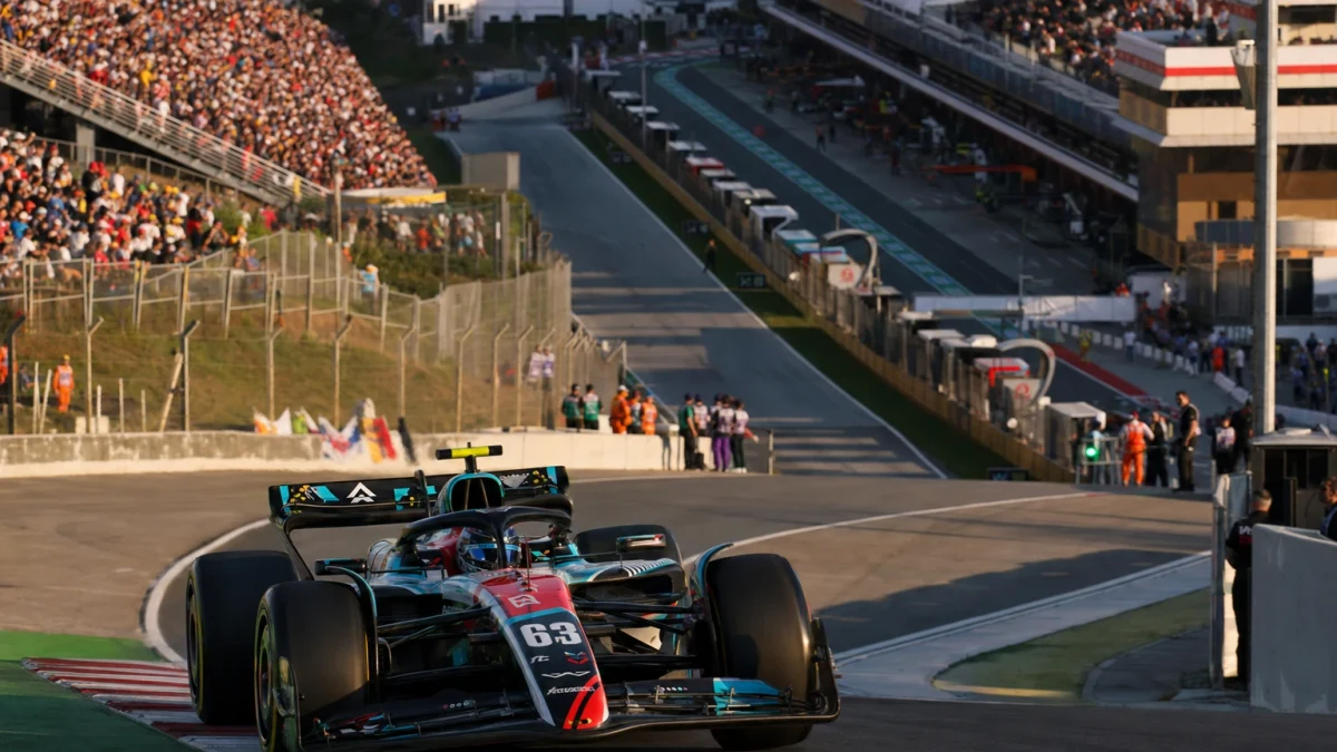 Formel 1-bil i silver som passerar mållinjen under kvalet på banan i Barcelona i kvällsljus.