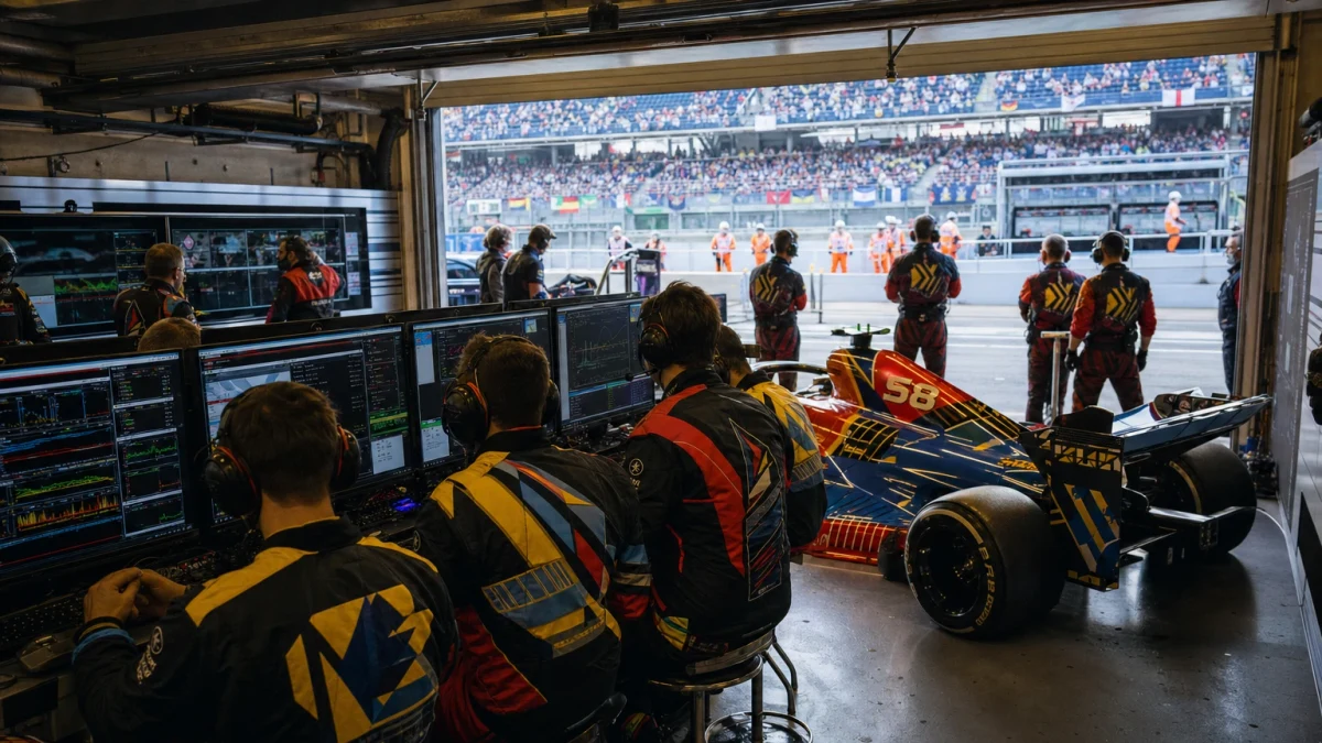 Ingenjör i teamklädsel lutad över en formel 1-bil i ett garage under en tävlingshelg.