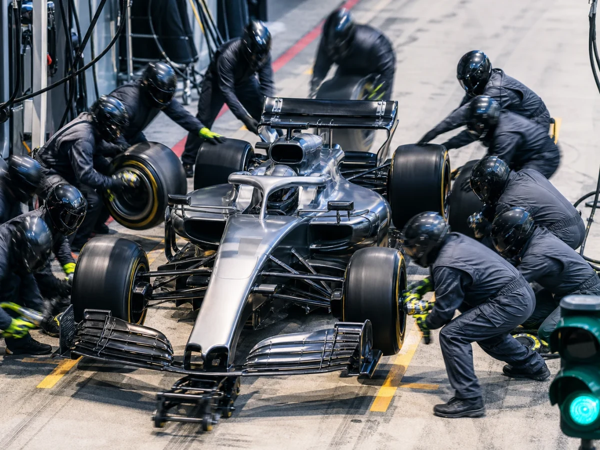 Formel 1-bil i depån med mekaniker runt om som byter alla fyra däcken samtidigt.